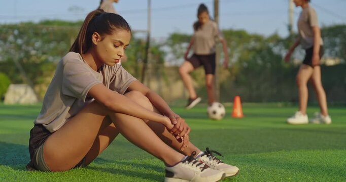 Indian asian happy athlete sad woman lady player group play football game kicking soccer ball enjoy team together at outdoor young adult gen z tired female girl sitting take break after practice - Powered by Adobe