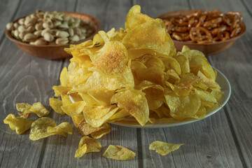assiette pleine de chips bien dorées avec pistaches et bretzels en arriere plan