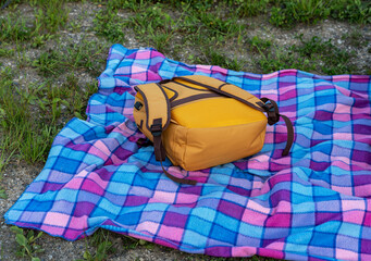 yellow backpack lying on checkered blue blanket on the ground, tourism and hiking concept, outdoor recreation