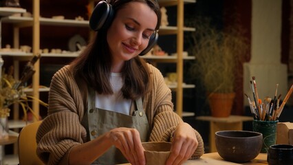 Caucasian relaxed woman girl female potter modeling clay process in workshop pottery hobby smiling sculptor designer listen music audio in headphones ceramics art therapy creating pot handmade craft