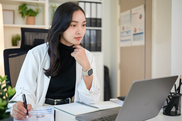 Focused businesswoman reviewing financial data and using laptop in a modern office.
