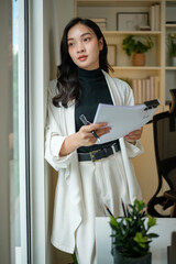 Thoughtful professional businesswoman in smart casual attire planning her tasks near a bright window.