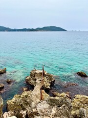 Vertical photo of rocky shore with weathered steps leading into clear turquoise sea, distant green...