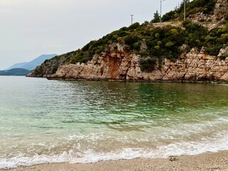 Rocky coastline with red and white cliffs, clear green sea, and gentle waves on pebble beach. Mediterranean Sea, summer vacation, travel, coastal landscape, Big Pebble Beach, Kas, Turkey. 