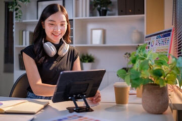 Woman in casual outfit holding a stylus and digital tablet, seated in a modern studio filled with swatches and monitors.