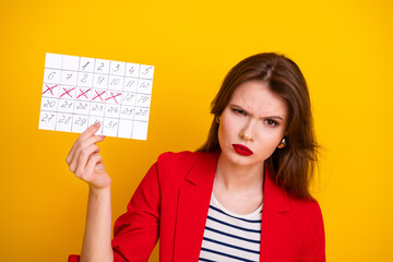 Confident young woman in a red blazer displaying a calendar against a vivid yellow backdrop