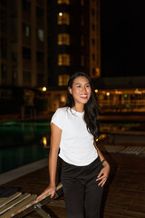 Portrait of young beautiful fashion model posing next to swimming pool during night