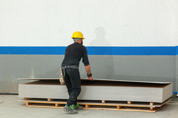 Construction worker picking plasterboard from pallet in warehouse