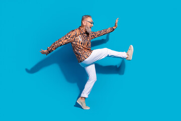 Fototapeta premium Stylish Mature Man Jumping in Joy Against a Vibrant Blue Background