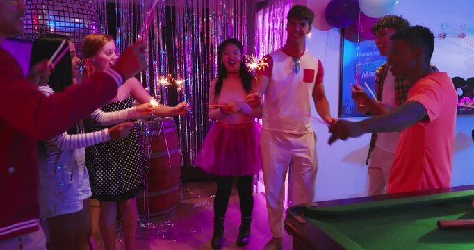 Diverse friends reacting to host sparkler light igniting and waving sparklers celebrating at party
