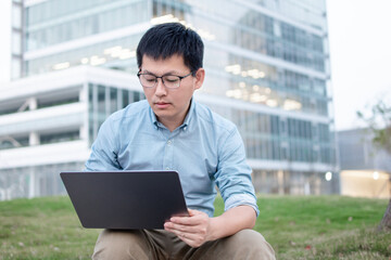 asain businessman working on laptop outside of office building