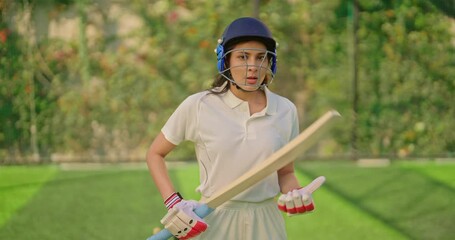 Indian gen z athlete sports woman lady standing at outdoor play ground wear white uniform and protective helmet looking at camera asian cricket player female girl hold bat day time at match playground - Powered by Adobe