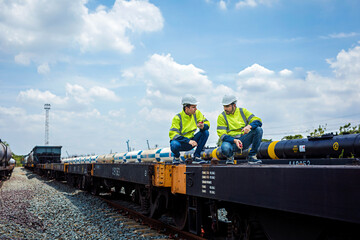 Teamwork, two male train engineers in reflective green and white hard hat holding walkie-talkie working at old train station with sky and clouds background.