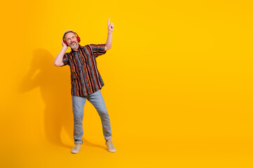 Stylish mature man dancing joyfully with yellow background wearing vibrant casual clothing and red...