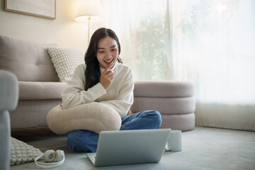 Fototapeta premium Happy young woman sitting comfortably on the floor with a laptop and headphones.