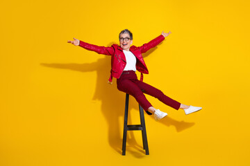 Cheerful elderly stylish woman in red leather jacket posed enthusiastically on a bright yellow...