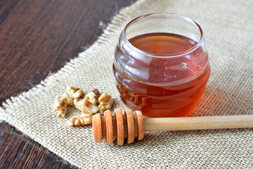 Honey jar with walnuts and a honey dipper on a burlap texture