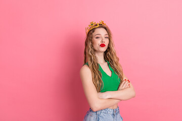 Stylish young woman in green top with crown posing confidently against pink background