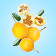 Delicious ripe passion fruits with green leaves falling on light blue background