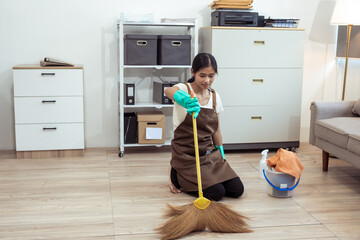 Young housekeeper wearing gloves and cleaning the table with a rag and cleaning spray. Professional...