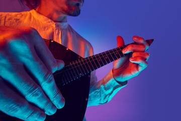 Close-up view of fingers plucking and fretting traditional string instrument with vibrant lighting...