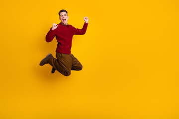 Young Man Jumping Cheerfully in Stylish Red Sweater on Yellow Background