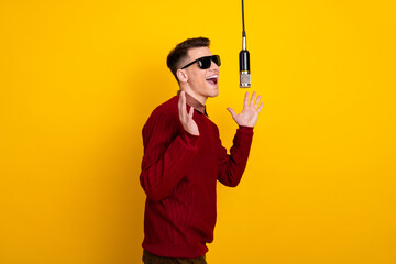 Handsome Young Man Singing Into Microphone Against Vibrant Yellow Background