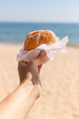 Bola de Berlim. Hand of a young woman holding a berliner on the beach. 
