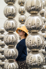 Woman in Yellow Hat Admiring Reflective Metallic Sphere Art Installation Display