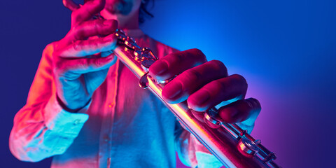 Man in white shirt playing silver flute under neon studio lighting against gradient background....