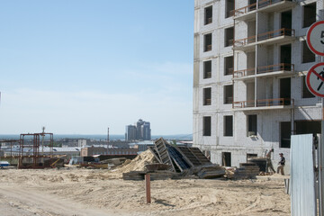 construction site near a large multi-storey grey brick apartment building with unglazed windows against the background of the city