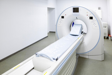A modern CT scanner  in Hospital. A computed tomography machine, with a patient table, and various auxiliary equipment and bright walls in a clean medical room on the basement floor of the facility.