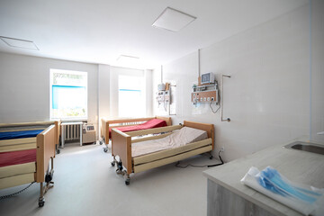 An oxygen hub with a flow meter and humidifier bottle is mounted on a wooden-paneled wall above a hospital bed in an intensive care unit