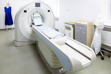 A modern CT scanner  in Hospital. A computed tomography machine, with a patient table, and various auxiliary equipment and bright walls in a clean medical room on the basement floor of the facility.