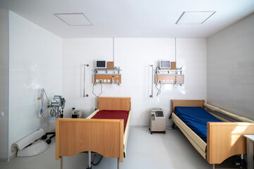 An intensive care ward for respiratory diseases features a red hospital bed, a lung ventilator, an oxygen concentrator, and an oxygen hub panel on a white wall.