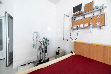 An intensive care ward for respiratory diseases features a red hospital bed, a lung ventilator, an oxygen concentrator, and an oxygen hub panel on a white wall.