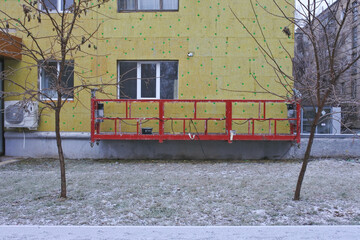 dirty red facade hoist near the insulated facade of the building