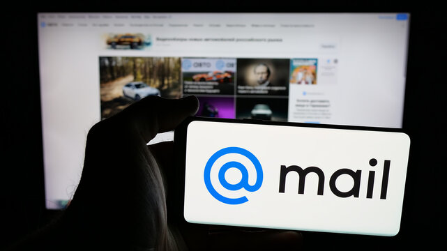Stuttgart, Germany - 05-27-2025: Person holding mobile phone with logo of Russian technology company Mail.ru on screen in front of web page. Focus on phone display.