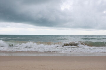 Big waves crashing against the beach with great force, splashing water. A view of the sea with strong waves on a sunless evening and a gloomy sky. The atmosphere looks like it's going to rain.
