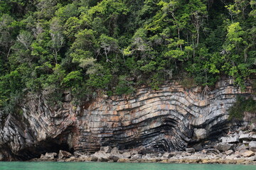 Series of layered stone slabs (Sedimentary Process) covered with lush green forest and blue sea. Geological wonders :The rock formation found in middle of Khanom Sea in Thailand.  Pancake Rock 
