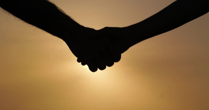 Silhouette closeup child and adult shaking hands at sunset, symbolizing mentorship, growth, trust. Powerful visual metaphor for guidance, personal development, generational support.