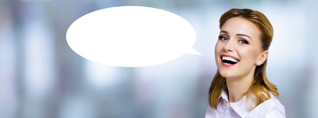 Wow! Portrait image of expressive emotional smiling young business woman with white empty mockup speech bubble. Happy cheerful cute blond hair girl against blurred modern office background