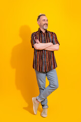 Fototapeta premium Stylish mature man posing confidently in vibrant retro outfit on bright yellow vertical background, exuding happiness and charisma