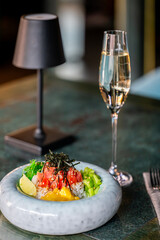A gourmet poke bowl with fresh diced tuna, seaweed, cucumber, mango, and rice, garnished with sesame seeds and a lime wedge, served alongside a glass of champagne on a stylish table setting