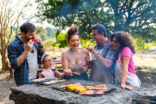 Happy fun family enjoying picnic in the woods on barbecue – family grilling in sunny backyard coocking meal on barbecue