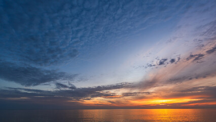 Sunset sky clouds over sea water background in evening with orange, blue sun light, Horizon sea ocean sunrise sky landscape nature backgrounds and gold sun down in golden hour summer season, Dusk sky