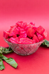 Diced beets in a glass bowl on a reddish-pink background