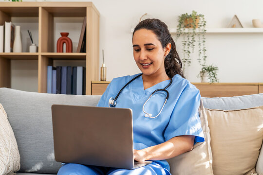 In a cozy living room, a healthcare professional or nurse sits on a sofa, diligently typing on a laptop late in the evening.