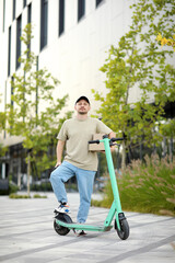 Man in casual clothes near parked electric scooter, delivery cardboard boxes on greened street in business area, look at camera. Concept of sustainability, delivering and eco-friendly modern lifestyle