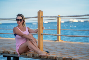 Woman sitting on a wooden bridge near the sea in a pink dress